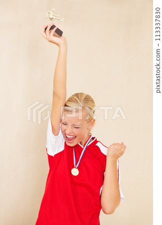 Woman, soccer player and trophy or a winner celebrate on a plain background for football achievement. A young female sports person or athlete with fist and champion medal award for winning a game Woman, soccer player and trophy or a winner celebrate on a plain background for football achievement. A young female sports person or athlete with fist and champion medal award for winning a game 113337830