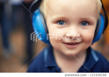 Baby, closeup and smile for portrait with headphones for noise at outdoor festival, happy and cute kid. Natural, blue and eyes with zoom face, toddler and innocent alone at concert for fun time 113338198