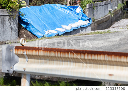 A house damaged by a natural disaster. Blue tarps and sandbags are placed over the collapsed area. 113338608