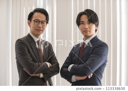 Two young men in suits with their arms folded Two young men in suits with their arms folded 113338630