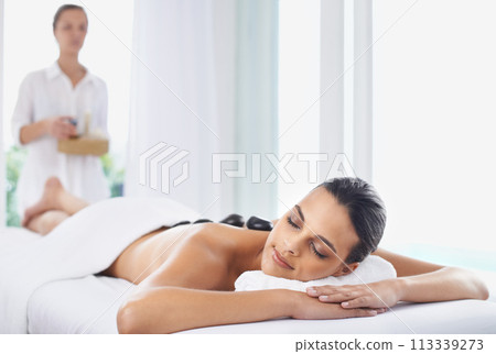 Hot stone, massage and woman at spa to relax, beauty and pamper back for wellness at luxury salon. Therapist, rocks and person in treatment for skincare, peace or calm for healthy body with masseuse 113339273