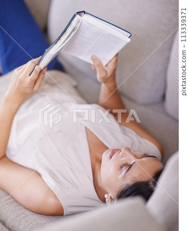 Woman, hobby and relax on sofa with book, reading and learning with story and literature entertainment at home. Happy, female person in living room with fiction or novel on couch for leisure 113339371