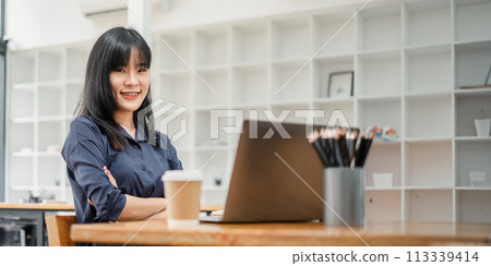 Professional young businesswoman sitting confidently at a cafe table with her laptop, ready for a productive work session. 113339414