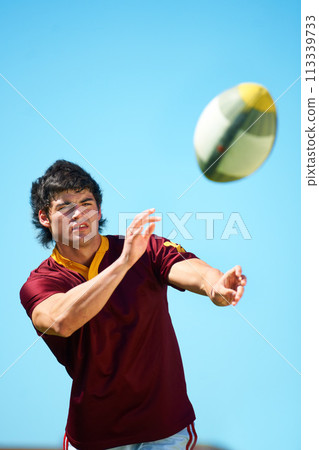 Sport, ball and male rugby player catching in training on a blue sky background. Professional athlete, uniform and confident fit exercise or workout for fitness game with a sportsman outdoors 113339733