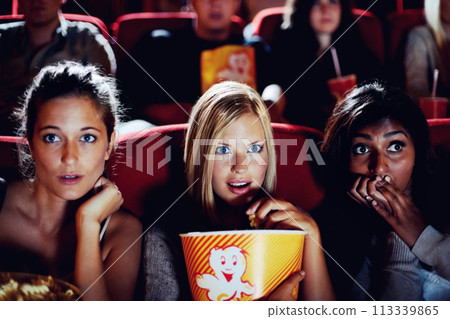 Wow, popcorn and women in the cinema watching a movie for entertainment while eating a snack. Face, expression and food with shocked young friends in a theater audience to experience a film together Wow, popcorn and women in the cinema watching a movie for entertainment while eating a snack. Face, expression and food with shocked young friends in a theater audience to experience a film together 113339865