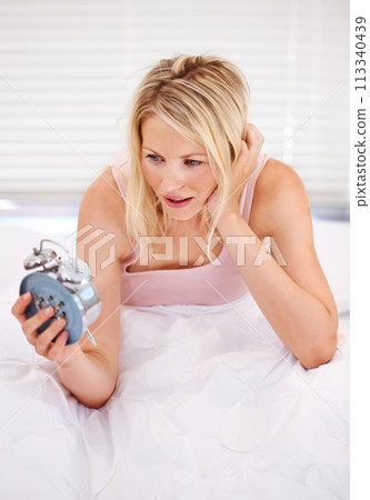 Woman, alarm clock and lazy for waking up in bed, tired and sleepless or fatigue at home. Female person, exhausted and pressing or hit snooze in apartment, frustrated and annoyed or late and anxious 113340439