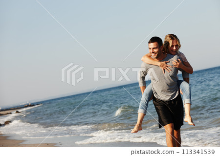 Couple, ocean water and piggyback on vacation, smile and peace at beach or game by blue sky. People, happy and tropical island for bonding on weekend, outdoor nature and love for marriage or romance 113341539