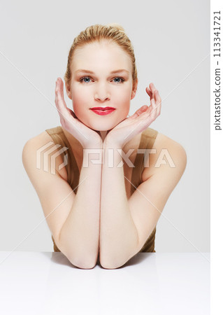 Portrait, skincare and woman in makeup at table, red lipstick and cosmetics in studio isolated on a white background. Face, beauty model and hands in spa facial treatment, wellness or healthy glow 113341721