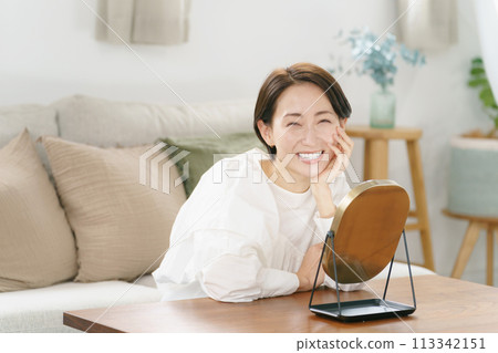 Woman smiling in the mirror in the living room Woman smiling in the mirror in the living room 113342151