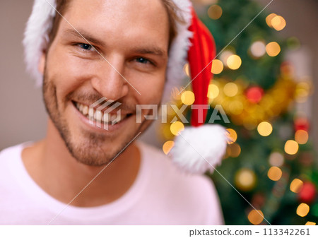 Man, party hat and portrait by Christmas tree, celebration and smiling at home on religious holiday. Male person, happy and special decoration for festive vacation, tradition and cheerful for event 113342261