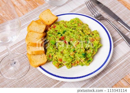 Portion of fresh guacamole with rusks served on table 113343114