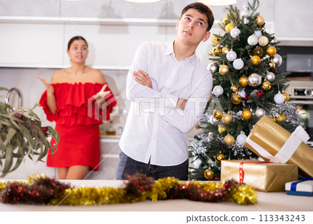 Annoyed young male and female getting mad at each other while standing near of Christmas tree in apartment 113343243