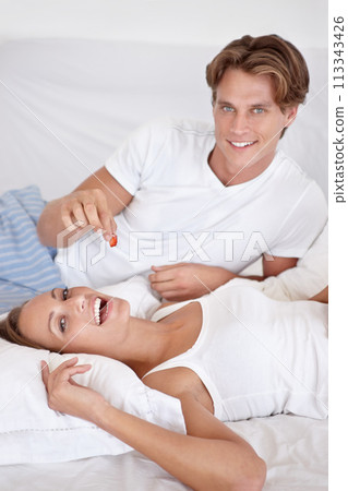 Couple, portrait and eating fruit in bed for romantic morning breakfast, honeymoon or relationship care. Man, woman and berry feed in apartment for hungry or house comfort or food, love or connection 113343426
