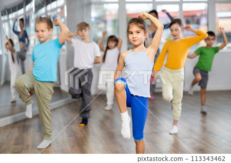 Positive juvenile girl engaged in hip-hop dance in training room with children's group Positive juvenile girl engaged in hip-hop dance in training room with children's group 113343462
