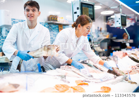 Positive salesman demonstrating cod in fish store 113343576