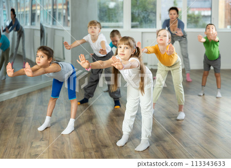 Positive juvenile girl engaged in Rock 'n' Roll dance in training room with children's group Positive juvenile girl engaged in Rock 'n' Roll dance in training room with children's group 113343633