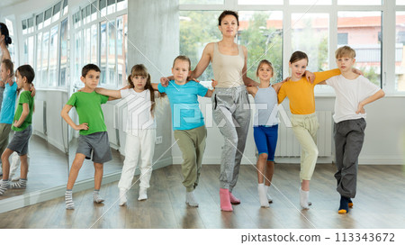 Smiling preteen children learning to dancing folk dance in row in studio 113343672
