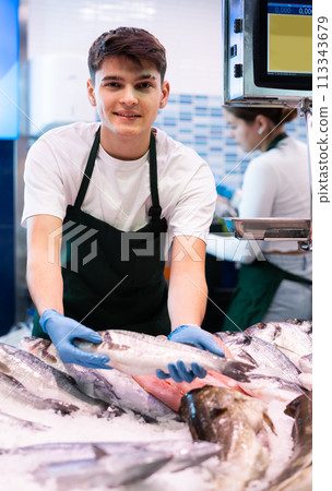 Smiling salesman demonstrating seabass in fish store Smiling salesman demonstrating seabass in fish store 113343679