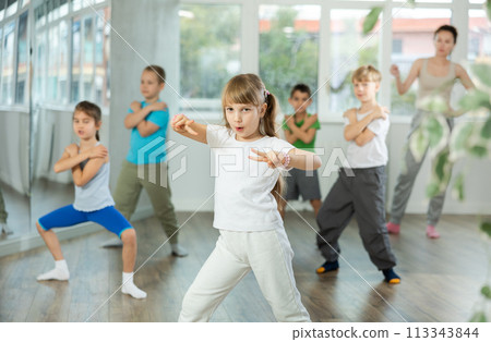 Positive juvenile girl engaged in breakdancing in training room with children's group Positive juvenile girl engaged in breakdancing in training room with children's group 113343844