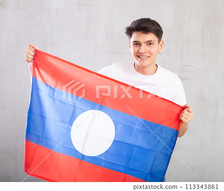 Reliant positive young man holds big national flag of Laos with confident smile showing teeth. 113343861