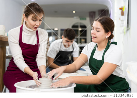Woman working with pottery wheel and master giving instructions 113343985