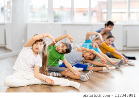 Little school age children learn to do dance moves on the floor in choreography studio Little school age children learn to do dance moves on the floor in choreography studio 113343991