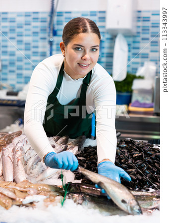 Positive saleswoman demonstrating trout in fish store 113343997