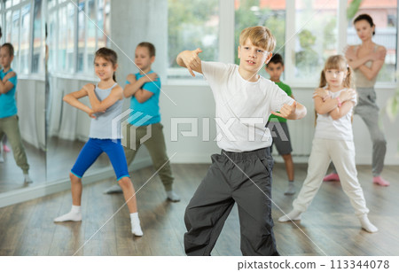 Children studying modern style dances with female teacher in dance class 113344078