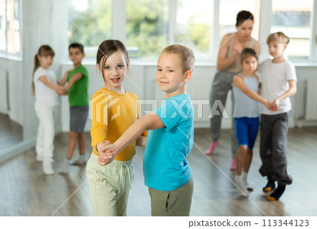 Preteen children learn to dance tango under guidance of a teacher in ballroom 113344123
