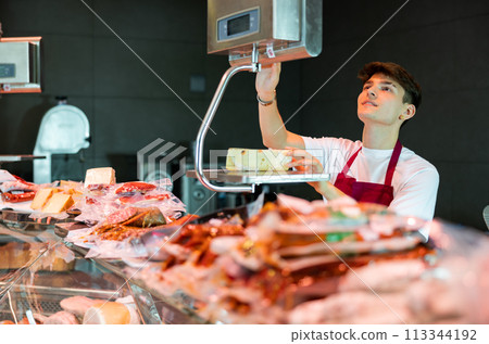 Young salesman weighing piece of fresh cheese in grocery store 113344192
