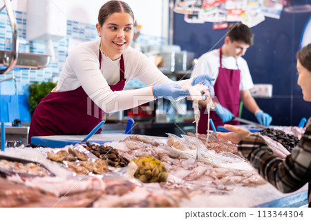 Positive saleswoman demonstrating calamary in fish store 113344304