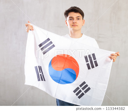 Focused young guy holding South Korea flag Focused young guy holding South Korea flag 113344382