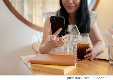 A cropped image of an Asian woman relaxing in a coffee shop and using her smartphone. A cropped image of an Asian woman relaxing in a coffee shop and using her smartphone. 113344488