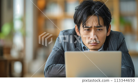 A businessman holding a head in front of a personal computer 113344650