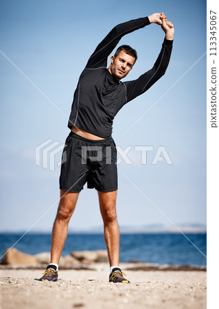 Man, stretching and beach on sand with shoes for health, fitness and exercise by ocean for peace and calm. Athlete, yoga and sea in morning for wellness, motivation and workout or training by nature 113345067
