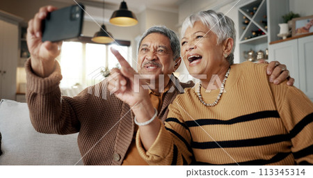Senior couple, selfie and happy on sofa, hug or talking for choice, check post and point for photography in home. Elderly woman, man and laugh with profile profile, web blog and social media on couch 113345314