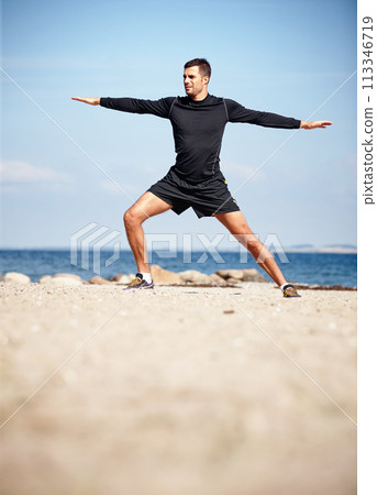 Athlete, stretching and beach on sand with shoes for health, fitness and exercise by ocean for peace and calm. Man, yoga and sea in morning for wellness, motivation and workout or training by nature 113346719