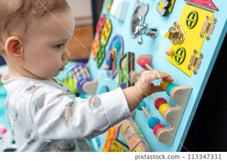 A baby moves wooden elements on a busy board 113347331