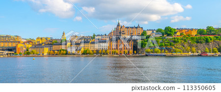 The warm sunlight bathes the historic buildings along the Sodermalm waterfront, with lush greenery accentuating the vibrant urban landscape against the serene waters. Stockholm, Sweden The warm sunlight bathes the historic buildings along the Sodermalm waterfront, with lush greenery accentuating the vibrant urban landscape against the serene waters. Stockholm, Sweden 113350605
