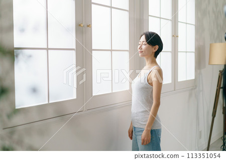 Middle-aged woman standing by the window 113351054