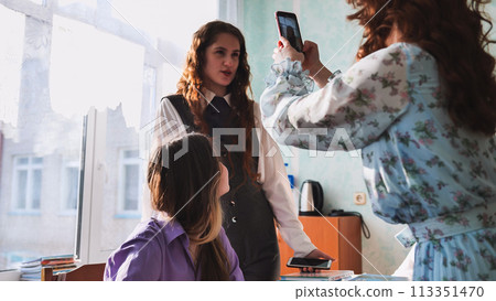 Schoolgirls taking photos of themselves on their phones in class. 113351470