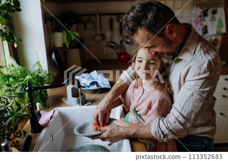 Dad and daughter washing dishes in sink together. Girls dad. Unconditional paternal love, Father's Day concept. 113352683