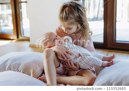 Portrait of big sister holding newborn sister. Girl carefully cuddling small baby. Sisterly love, joy for new family member. Portrait of big sister holding newborn sister. Girl carefully cuddling small baby. Sisterly love, joy for new family member. 113352685