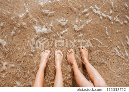 Close up of feet on beach with sea water beneath them. Sea foam and warm water soaking legs. Close up of feet on beach with sea water beneath them. Sea foam and warm water soaking legs. 113352732