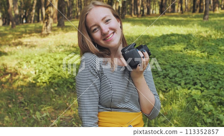 A young girl photographer with a camera poses in the park. A young girl photographer with a camera poses in the park. 113352857