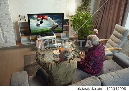 Elderly men, sport fans, friends sitting in living room at hoe, drinking beer and watching online football match translation 113354008