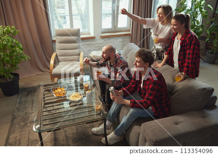 Emotional young people, friends gathering in living room at home, eating snacks, drinking beer and watching online football match translation 113354096