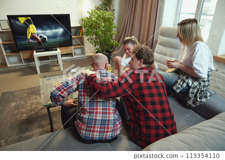 Young people, friends sitting on sofa at home in living room and watching online football match translation 113354110