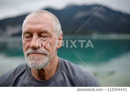 Portrait of active senior man resting after hiking in mountains. Thoughtful elderly man enjoying peaceful nature. 113354431