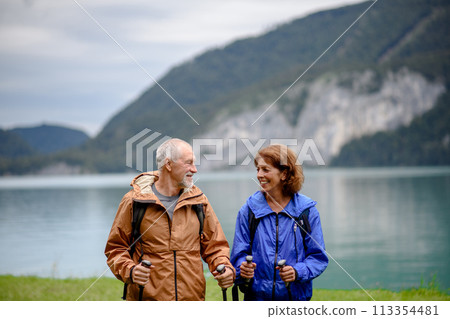 Portrait of beautiful active elderly couple hiking together in spring mountains. Senior tourists standing in front of lake. Portrait of beautiful active elderly couple hiking together in spring mountains. Senior tourists standing in front of lake. 113354481